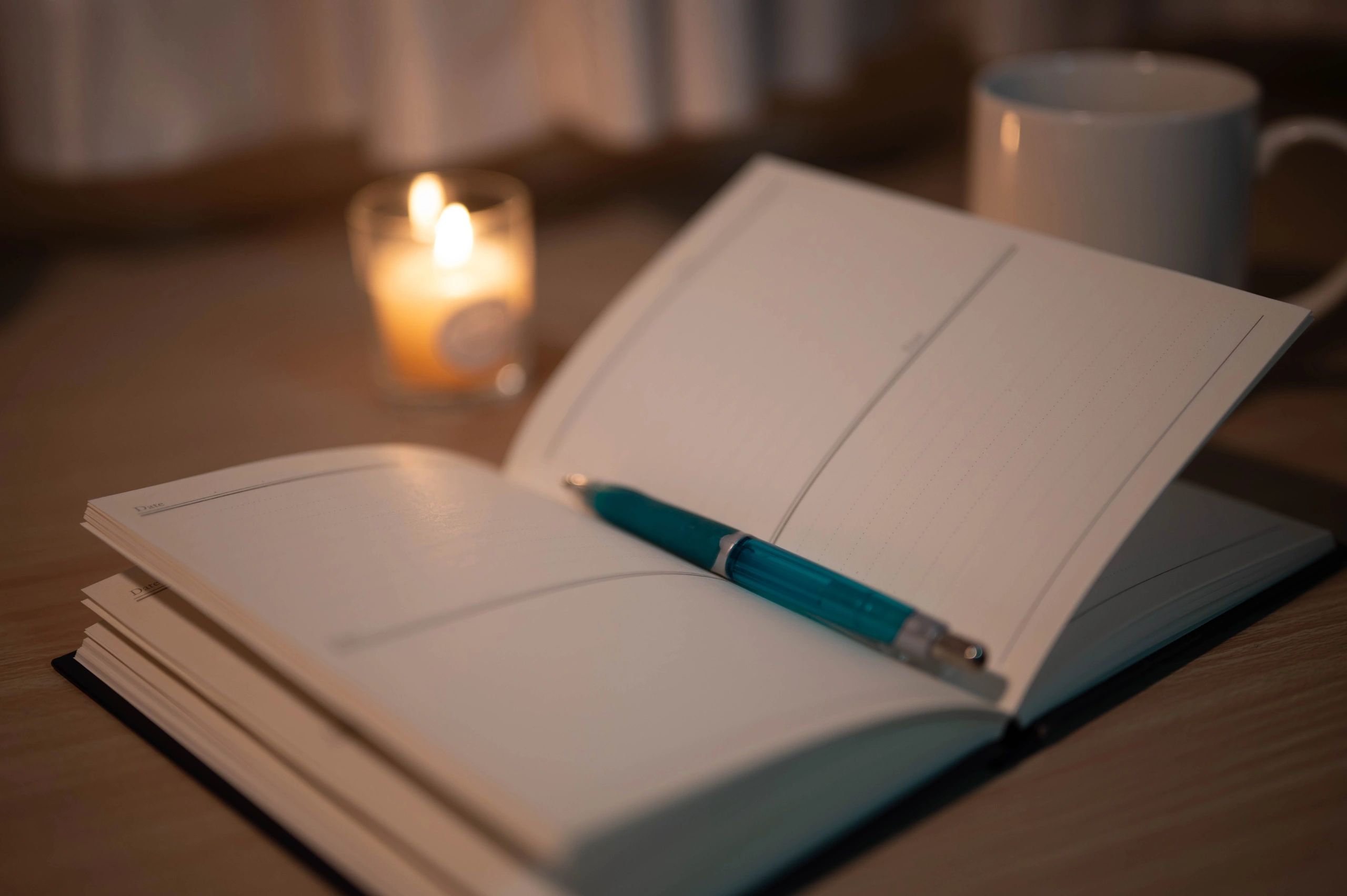 Notebook and pen on a desk with a lit candle and coffee cup